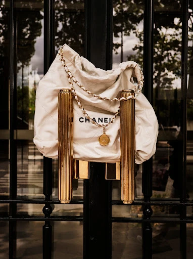 Chanel purse in dust bag with gold chain and medallion hanging on ornate black metal gate with fluted gold door handles.