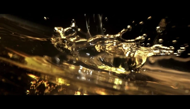 Golden liquid is captured mid-splash against a black background, highlighting fluid dynamics and the reflective qualities of the viscous fluid.