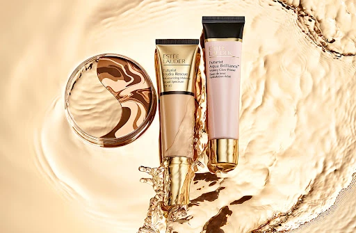 Estee Lauder skincare products on reflective gold surface: foundation compact, hydra rescue moisturizer, aqua brilliance primer, beauty.