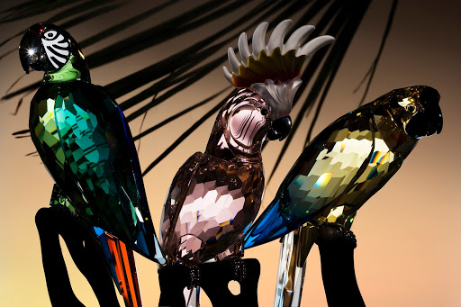 Three crystal parrot figurines are displayed against a soft background, showcasing their faceted details and vibrant colors under studio lighting.