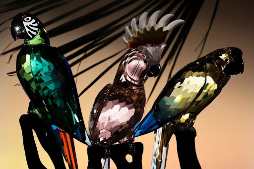 Three crystal parrot figurines are displayed against a soft background, showcasing their faceted details and vibrant colors under studio lighting.