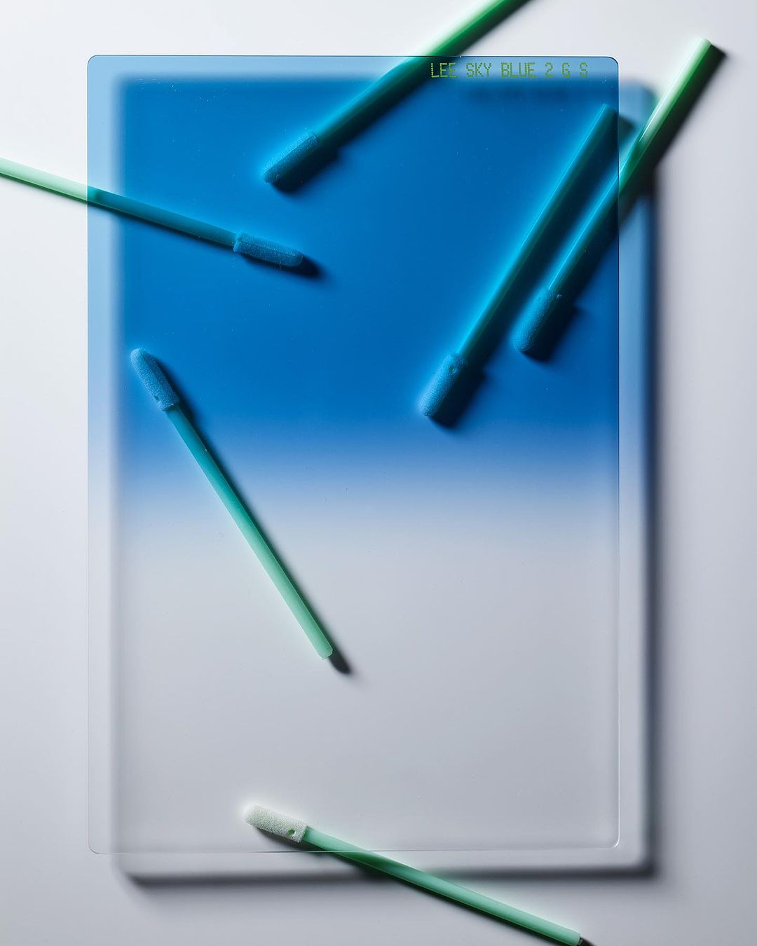 Abstract image features a gradient filter with a blue and white blend, accompanied by green cleaning wands spread across the surface.