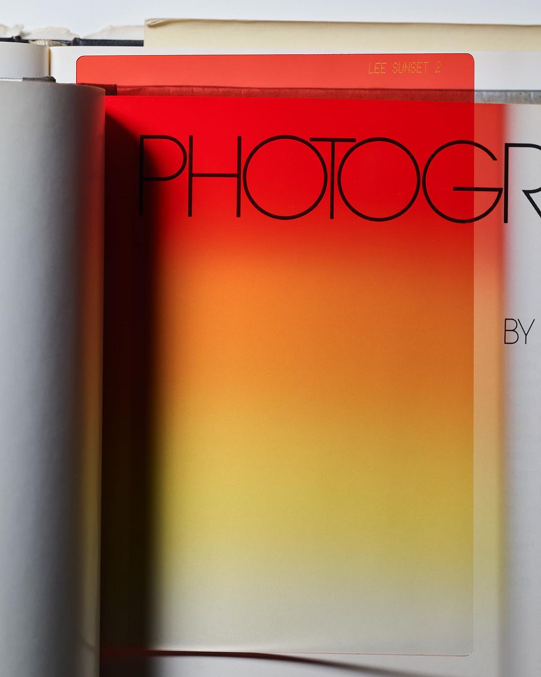 Close-up of a photography book with a red and yellow gradient filter overlaying the text. An open book and gray tube are visible.