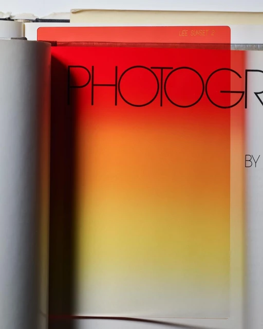 Close-up of a photography book with a red and yellow gradient filter overlaying the text. An open book and gray tube are visible.