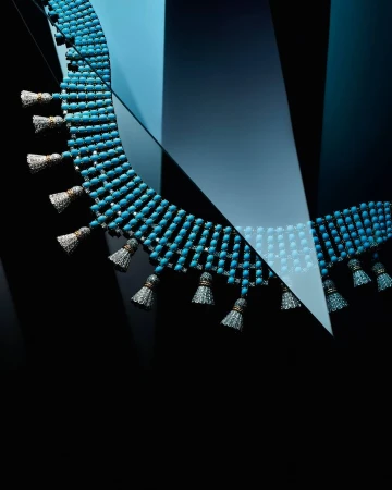 Necklace with turquoise beads and tassel details on a gradient blue to black background in a studio product shot for jewelry design.