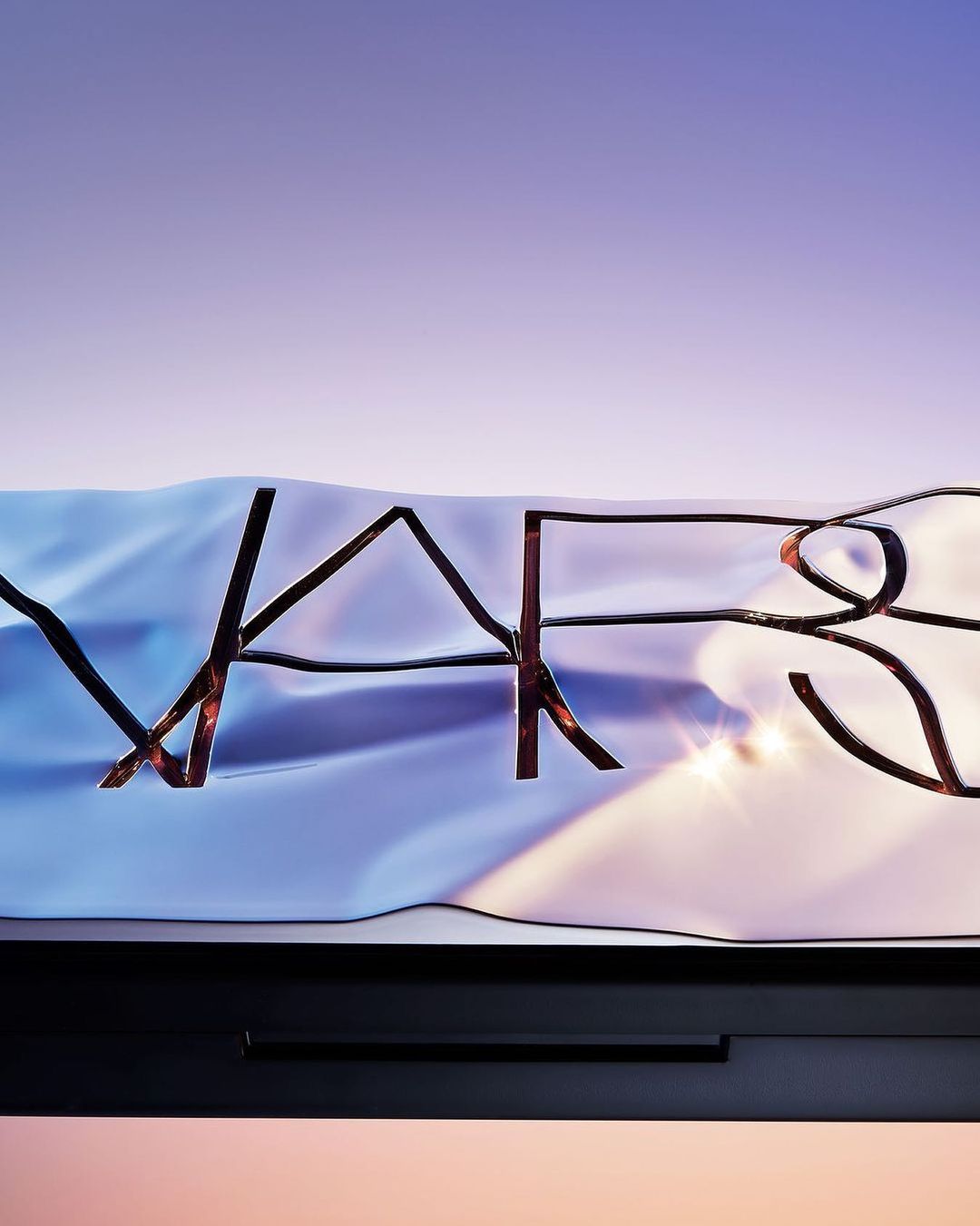Close-up of NARS product packaging featuring a compact case with the brand's name in raised, textured lettering on a wavy surface.