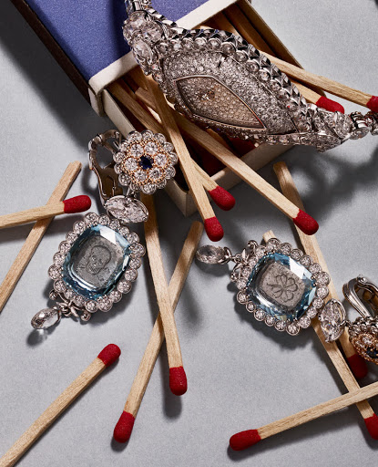 Close-up of diamond jewelry, including a necklace and earrings, nestled in a blue matchbox with scattered wooden matches.