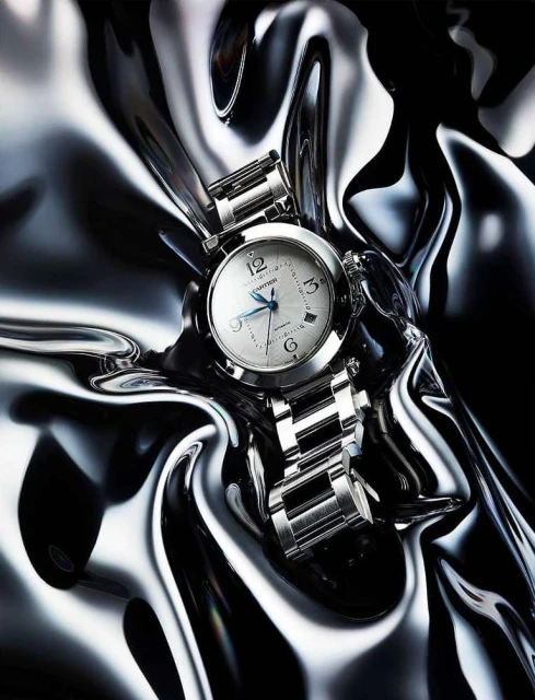 Silver wristwatch with a metal band displayed on a rippled dark metal background with highlights reflecting on the watch and material.