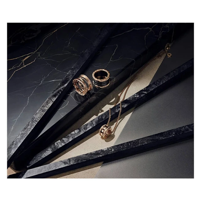 Luxury gold rings and a necklace are artfully displayed on a dark marble surface, highlighted by a beam of light. Jewelry.