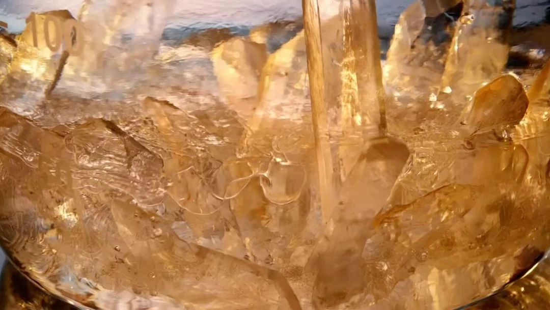 Close-up shot of golden liquid being poured over ice, filling the frame with a golden hue and textural details of frozen ice.
