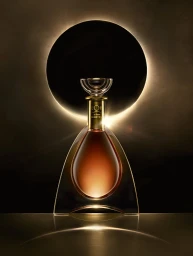 L'Or de Jean Martell decanter bottle positioned against a dark background featuring a glowing halo of light resembling a total solar eclipse.