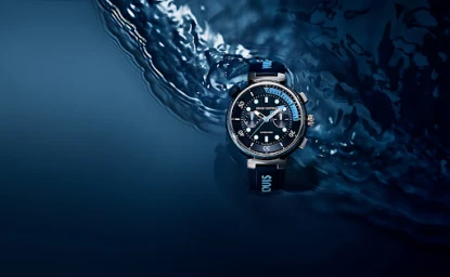 Luxury diving watch with black dial and dark blue strap submerged in rippling water under moody lighting