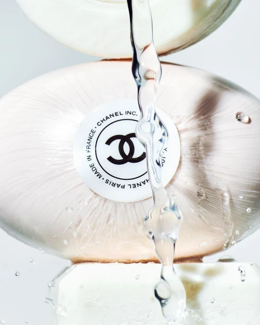 Close-up of a stack of three white Chanel soap bars with water running over them against a clean, bright background in a studio setting.