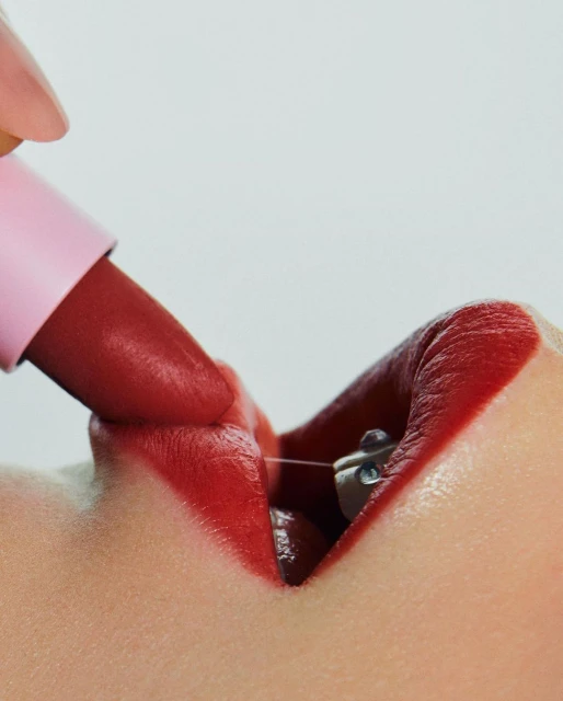 Close-up of a person's lips with bright red lipstick being applied from a pink-tubed lipstick applicator; beauty and makeup concept.