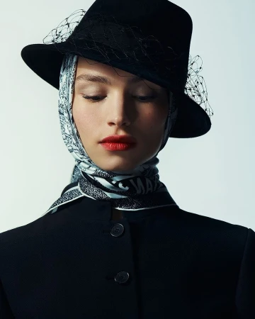 Close-up portrait of a woman wearing a black fedora hat with veil and patterned headscarf by Zoé Kovacs