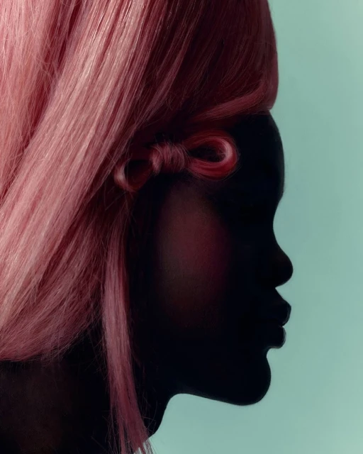 Close-up studio shot of a person's silhouette in profile with pink wig and bow detail against a light blue backdrop.