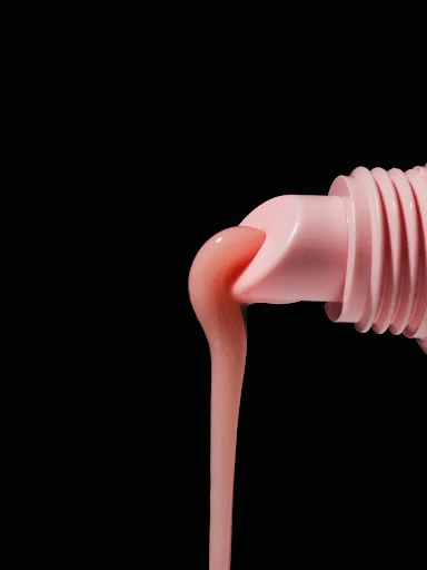 Close-up of pink liquid flowing from a pink tube against a black background, product shot, skincare, beauty product.