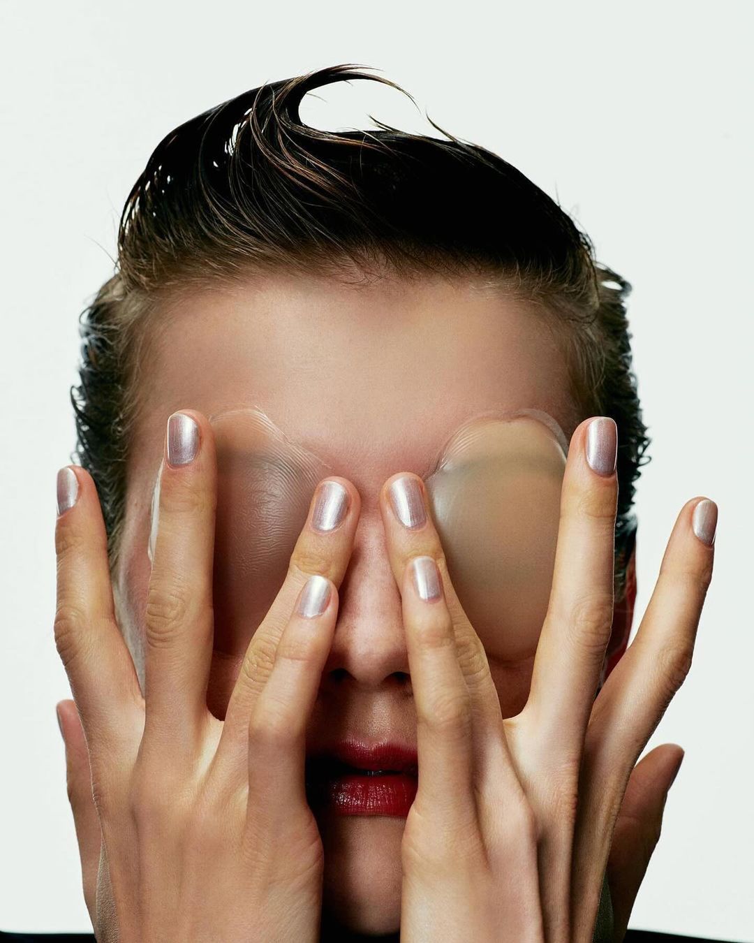Close-up portrait of a woman with wet hair using her hands and eye patches to cover her face in a beauty or wellness concept.