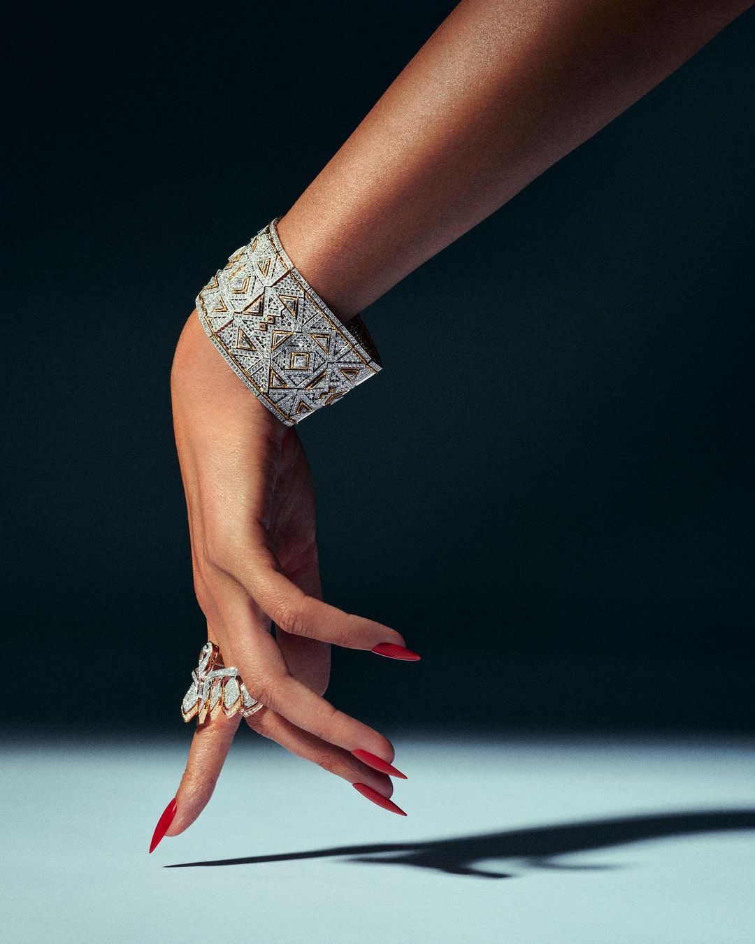 Close-up shot of an arm and hand adorned with an ornate diamond bracelet and ring, set against a dark background with a soft light.