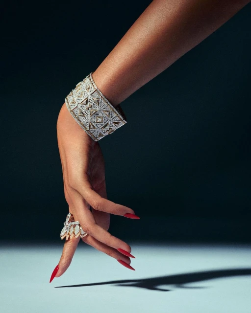 Close-up shot of an arm and hand adorned with an ornate diamond bracelet and ring, set against a dark background with a soft light.