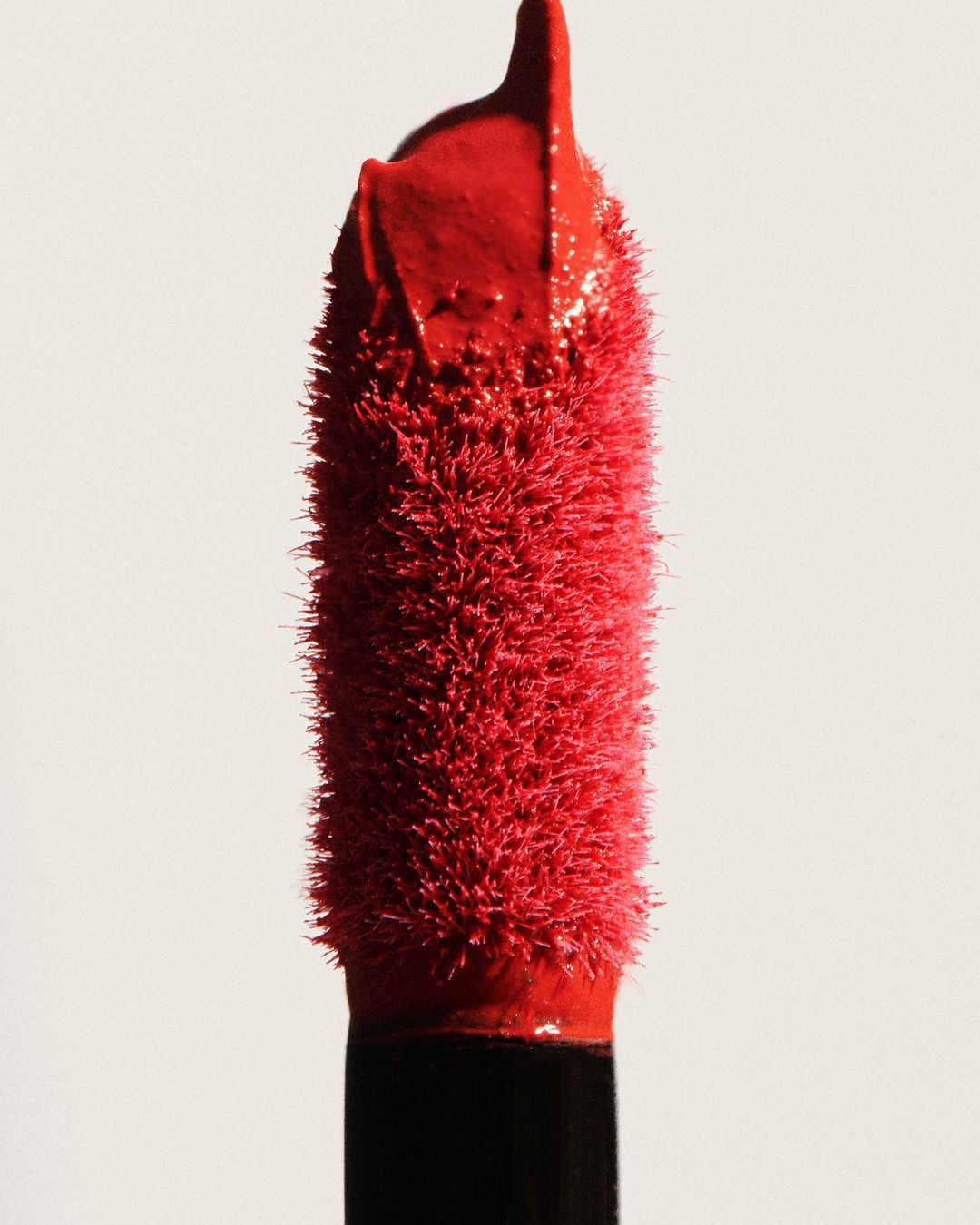Close-up of a red lip gloss applicator brush against a plain white background, highlighting the texture and color of the product.