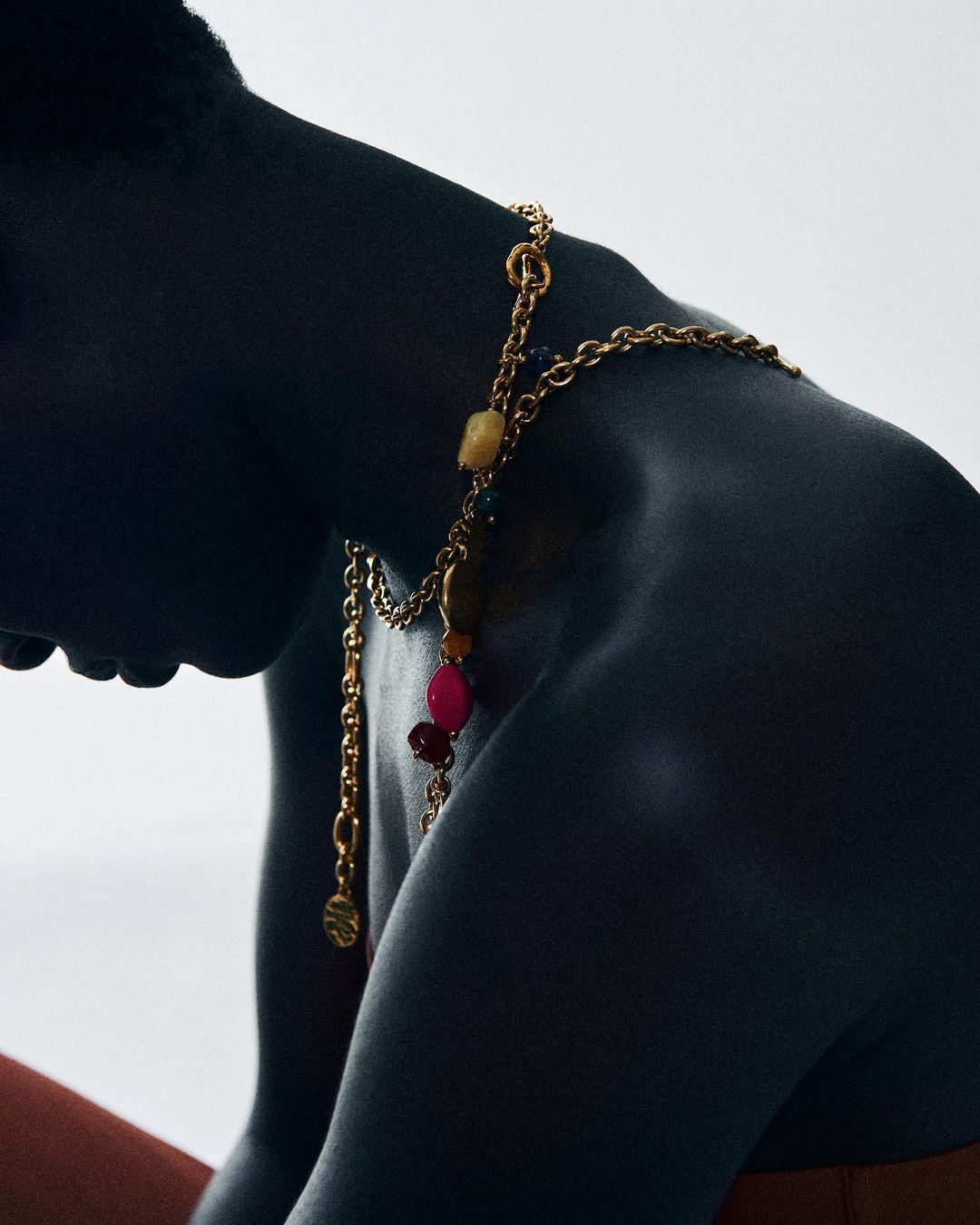 Close-up shot of an adult with dark skin wearing a gold beaded necklace, set against a soft white backdrop.