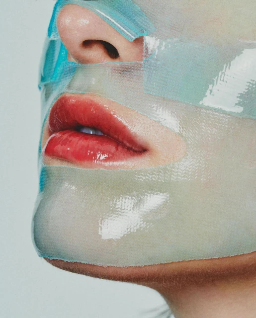 Close-up portrait of a person wearing a semi-transparent sheet mask, focusing on their glossy red lips and facial skincare treatment.