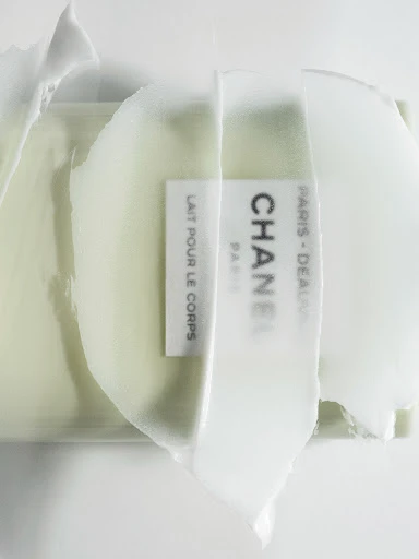 Close-up of Chanel body lotion showing its creamy texture and brand label in a studio setting against a bright white background.