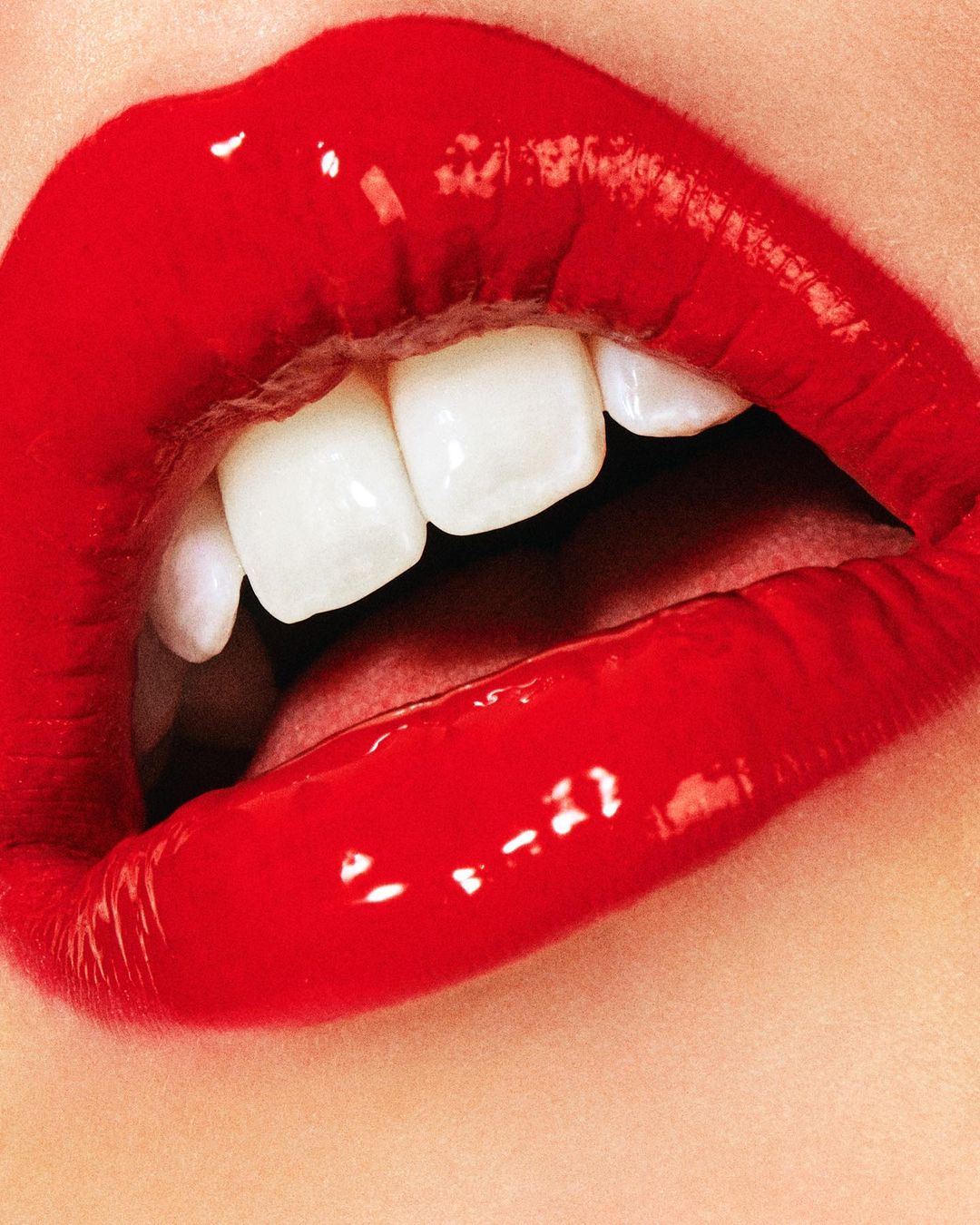 Extreme close-up of bright red glossy lips with white teeth visible. Focus on the vibrant color and texture of the mouth area.