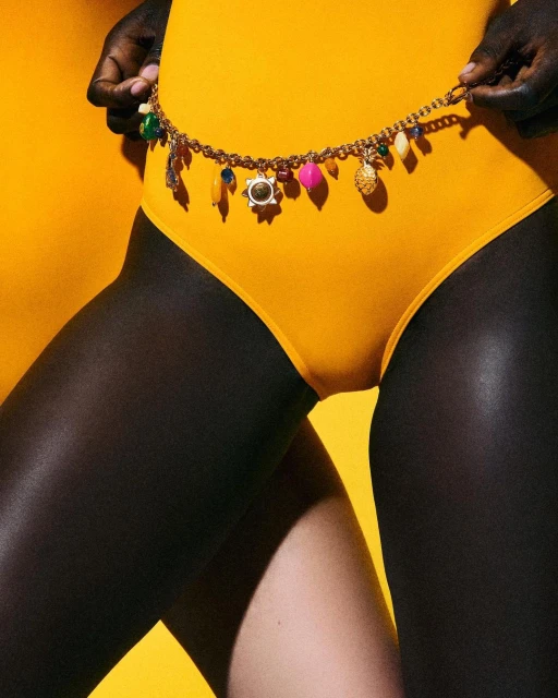 Close-up shot of a woman wearing a yellow swimsuit and a beaded belt against a yellow background, showing the texture and details.