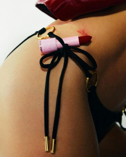 Close-up of a woman's body with a pink lipstick attached to her black bikini bottoms with gold hardware and red jacket.
