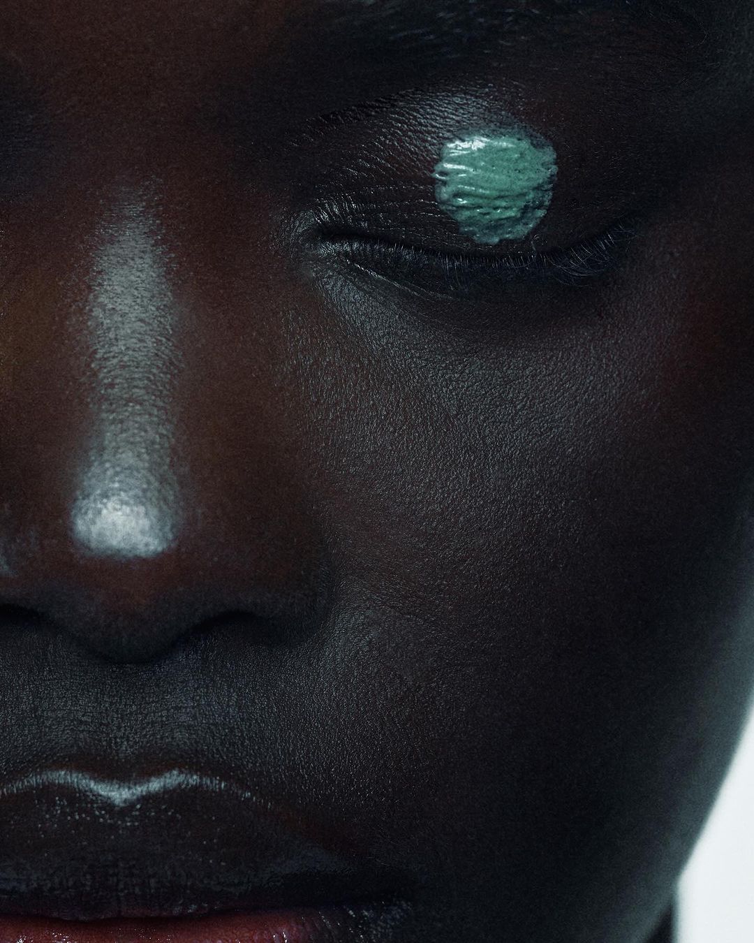 Close-up of a dark-skinned woman's face with an eye painted with a teal cosmetic color, showcasing beauty and body art.