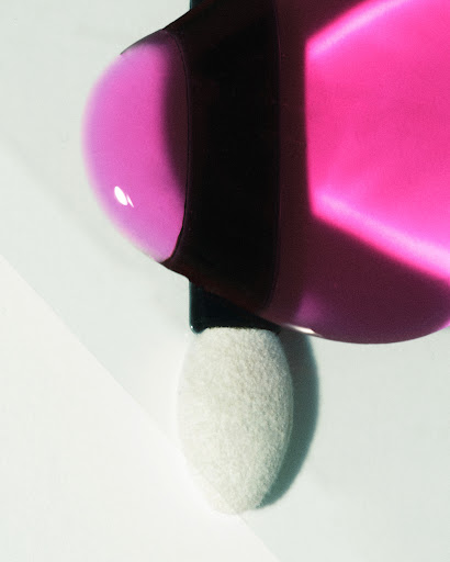 Close-up of a pink liquid cosmetic product with a sponge applicator, minimal composition and presentation on a white surface.