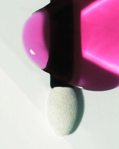 Close-up of a pink liquid cosmetic product with a sponge applicator, minimal composition and presentation on a white surface.