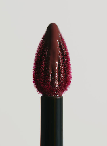 Close-up of lipstick applicator with dark red lipstick on a plain background showcasing beauty and makeup product for cosmetic use.