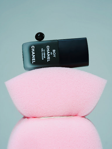 Elevated studio shot of black Chanel nail polish bottle with dark cap on pink sponge platforms, showcasing beauty product. 