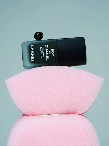 Elevated studio shot of black Chanel nail polish bottle with dark cap on pink sponge platforms, showcasing beauty product. 
