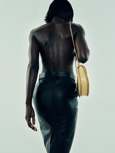 Back view of a slender African American woman in a black skirt with a cream-colored purse over her shoulder in a studio setting.