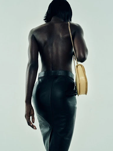 Back view of a slender African American woman in a black skirt with a cream-colored purse over her shoulder in a studio setting.