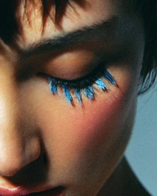 Close-up shot of a person's face with short brown hair, closed eye and artistic long blue eyelashes. Beauty shot, make-up.