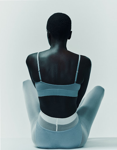 Back view of a Black female model in a light blue sports bra and leggings against a white backdrop in a fashion studio.