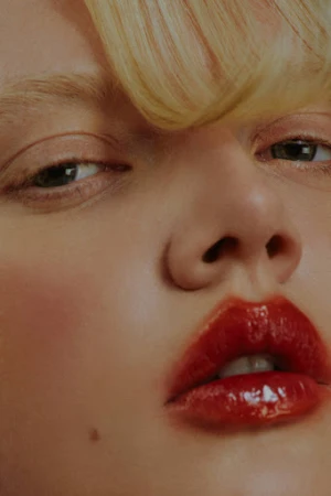 Close up beauty portrait of a woman with glossy red lips and blonde fringe by Zoé Kovacs.