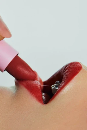 Close-up macro shot of red lipstick being applied to lips wearing dental braces, against a clean white background.