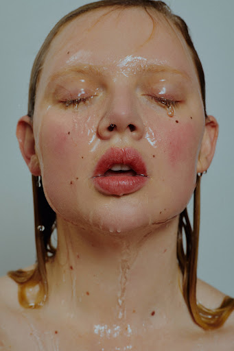 Close-up portrait of a woman with wet skin, slicked hair, and closed eyes against a neutral background by Zoe Kovacs