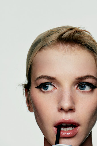 Close-up of an adult female drinking with a straw, showcasing makeup and beauty in a studio setting with a bright, clean aesthetic.