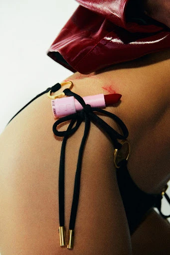 Close-up shot of the midsection of an adult female, adorned with a tube of lipstick tied to the waist with a black string.