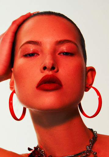 Close-up portrait of a model with a red color grade, featuring red lipstick, red hoop earrings, and a silver chain necklace.