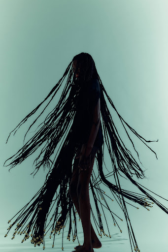 Striking fashion portrait of a Black female model with elaborate braided hair, against a pale teal backdrop, showcasing beauty and style.