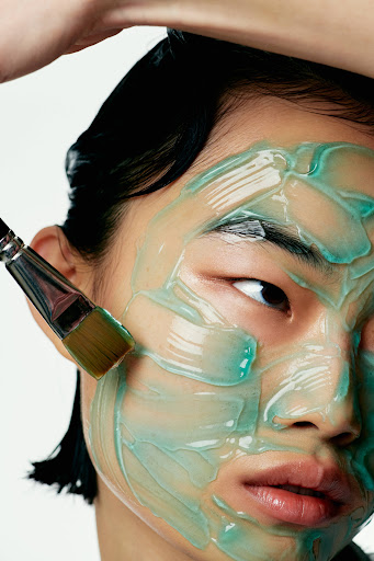 Close-up of a person's face covered with a blue face mask being applied with a brush in a beauty or skincare context.
