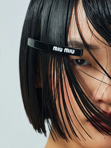 Close-up shot of a woman with short black hair and a black hair clip with the brand name Miu Miu in white letters.